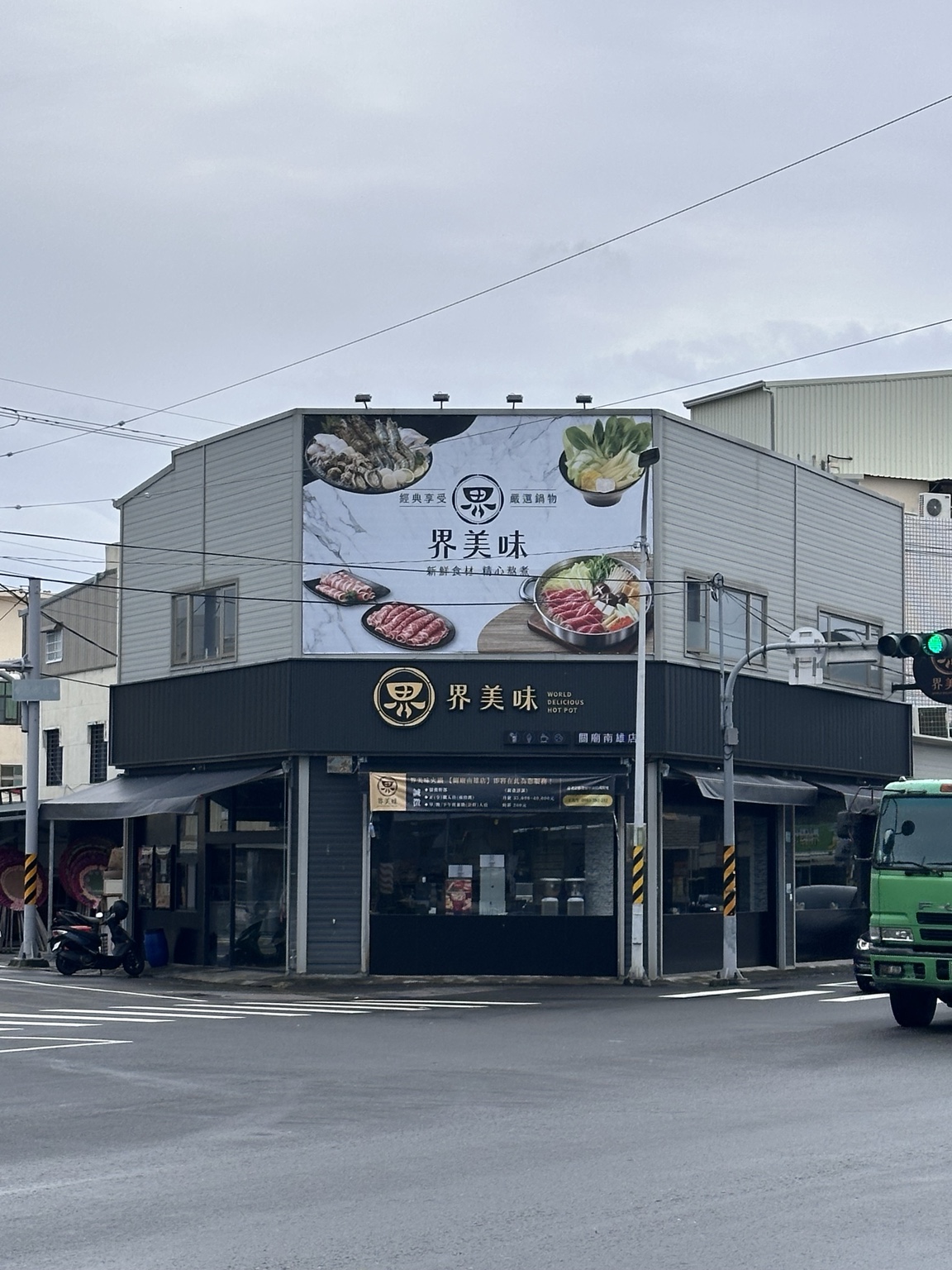 從路口遠看界美味關廟南雄店大型帆布與延伸至兩側的企口板門面
